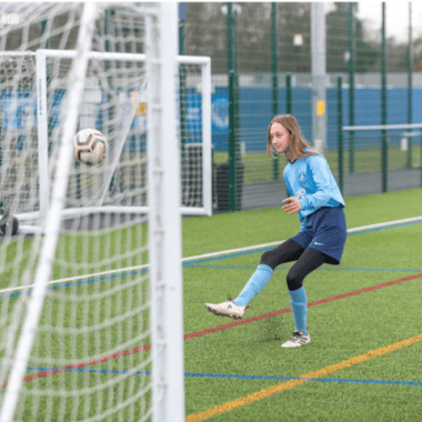 Action shot of teenage female kicking ball into a goal on YMCA Newark Village pitch