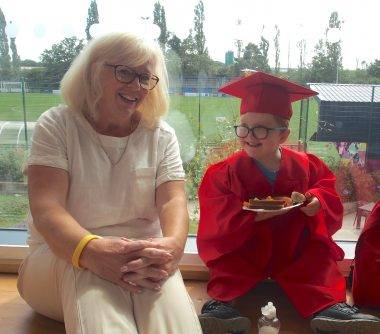 Cath Shotton is sat alongside a child graduating Nursery